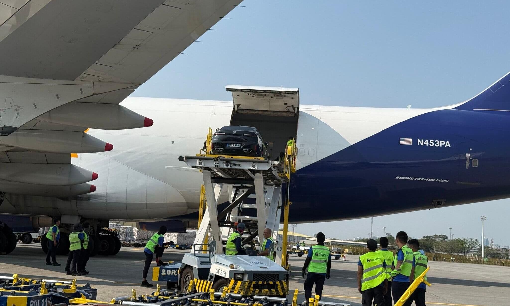 Vehículo de lujo en una plataforma de carga junto a un avión carguero
